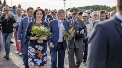 Sauli Niinistö och Jenni Haukio går med blommor i handen bland folket på Gullranda.