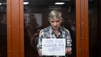 Vid förhandlingen i rättssalen visar Alexei Gorinov en lapp bakom en glascell där det står: "Behöver ni fortfarande det här kriget?"
