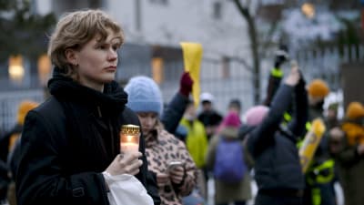 En person håller i ett tänt gravljus vid protesten utanför den ryska ambassaden i Helsingfors.