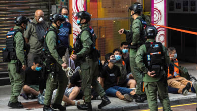 Poliser på gata i Hongkong, på marken sitter unga personer.