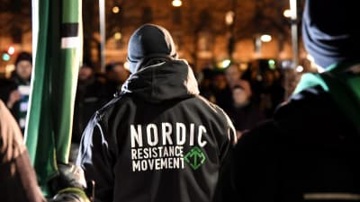 Nordiska motståndsrörelsens marsch i Helsingfors på självständighetsdagen 2017. En man har på sig en jacka med organisationens namn tryckt på ryggen.