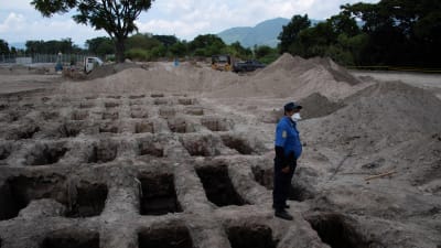 En polis i El Salvadors huvudstad San Salvador vid nygrävda gravar för pandemioffer. Bilden är tagen den 27 juli. 