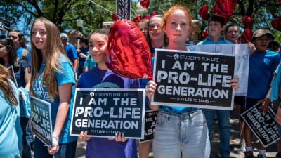 Tre flickor deltar i en demonstration mot abort, i bakgrunden fler deltagare.