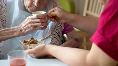 Närvårdare hjälper äldre person att äta. 