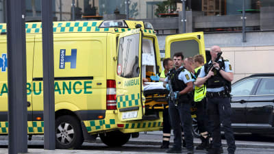 Tungt beväpnade poliser som står runt en ambulans, i vilken man lastar in en person.