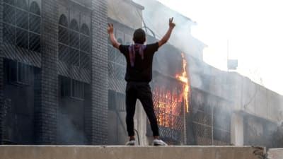 En demonstrant står utanför en brinnande statlig byggnad