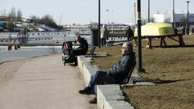 Man klädd i svart sitter på parkbänk vid Eira strand och solar sig i vårsolen. 