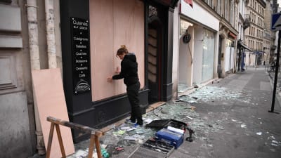 En kvinna i Paris ersätter ett krossat skyltfönster med plywoodskivor på söndag morgon. 