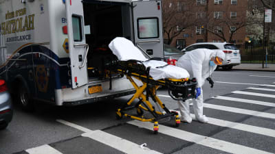 En ambulansförare i skyddsdräkt torkar av en bår utanför ett sjukhus i New York