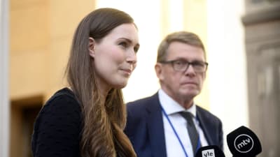 Statsminister Sanna Marin och finansminister Matti Vanhanen står bredvid varandra på Ständerhusets trappa och svarar på journalisternas frågor i mikrofoner.