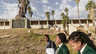 Skolflickor i Namibia Juni 2017. I bakgrunden ett monument till minne av dem som blev offer för det folkmord som Tyskland begick i början av 1900-talet.