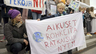 En liten pojke håller upp ett lakan med texten "Vuxna, modiga beslut nu!"