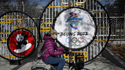 En dam cyklar framför OS-rekvisita i Peking.
