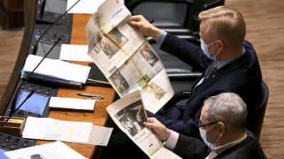 Samlingspartister i riksdagens plenisal läser gamla tidningar.