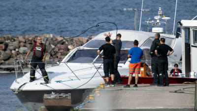 Större motorbåt vid brygga men människor kring och på båten. Olycksbåtarna på Erstan den 3 augusti 2019 transporterades till Pärnäs i Nagu.