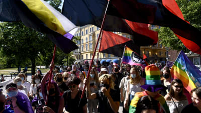 prideparaden där demonstranter viftar med stora flaggor.