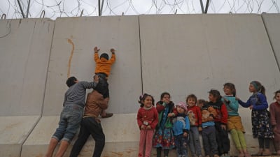 Syriska flyktingbarn klättrar vid en gränsmur som Turkiet byggt mot den syriska byn Kafr Lusin, i Idlib.