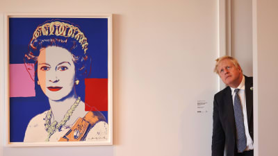 Boris Johnson kikar in genom en dörr och sneglar upp mot taket. Bredvid honom ett stort porträtt på drottning Elizabeth.
