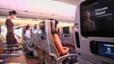 Tomma bänkrader i ett flygplan. Selektivt fokus på en skärm fäst på ett säte. I bakgrunden ser man flera tomma platser i flygplanet.