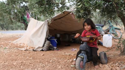 Ett barn som flytt undan striderna i södra Idlib leker utanför ett tält