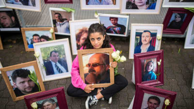 En flicka sitter på marken omringad av porträtt av offer för den Syriska regimen.