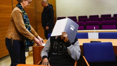 En man täcker sitt ansikte med en pärm i en rättegångssal. 