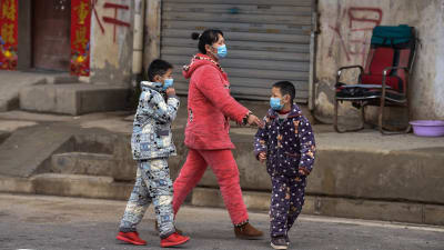 På bilden syns en mamma med sina två barn promenera i Wuhan iklädda ansiktsmasker.