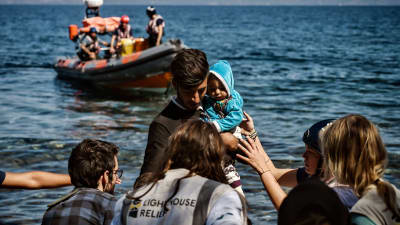 Migranter som anländer 16.9.2019 till Lesbos från Turkiet. I bildens mitt ses en man med ett spädbarn, i bakgrunden en ribbåt. 