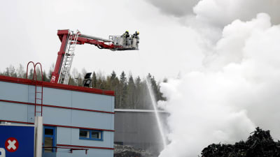 Vattenstråle riktas från en lyftkran ner mot ett moln av brandrök. Brandmän arbetar under en eldsvåda i Tammerfors den 11 maj 2020.