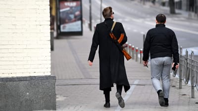 Två män går längs en gata. Den ena mannen bär ett vapen över axeln.
