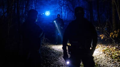 Poliisit valaisevat taskulampuilla pimeää metsää.