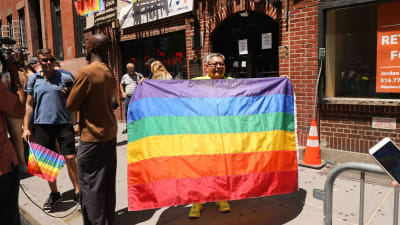 En person håller upp en regnbågsflagga utanför baren Stonewall Inn i New York.
