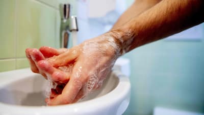En person tvättar händerna i ett handfat.