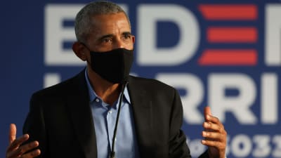 USA:s tidigare president Barack Obama talar med händerna i luften. Han har ett svart munskydd på sig.