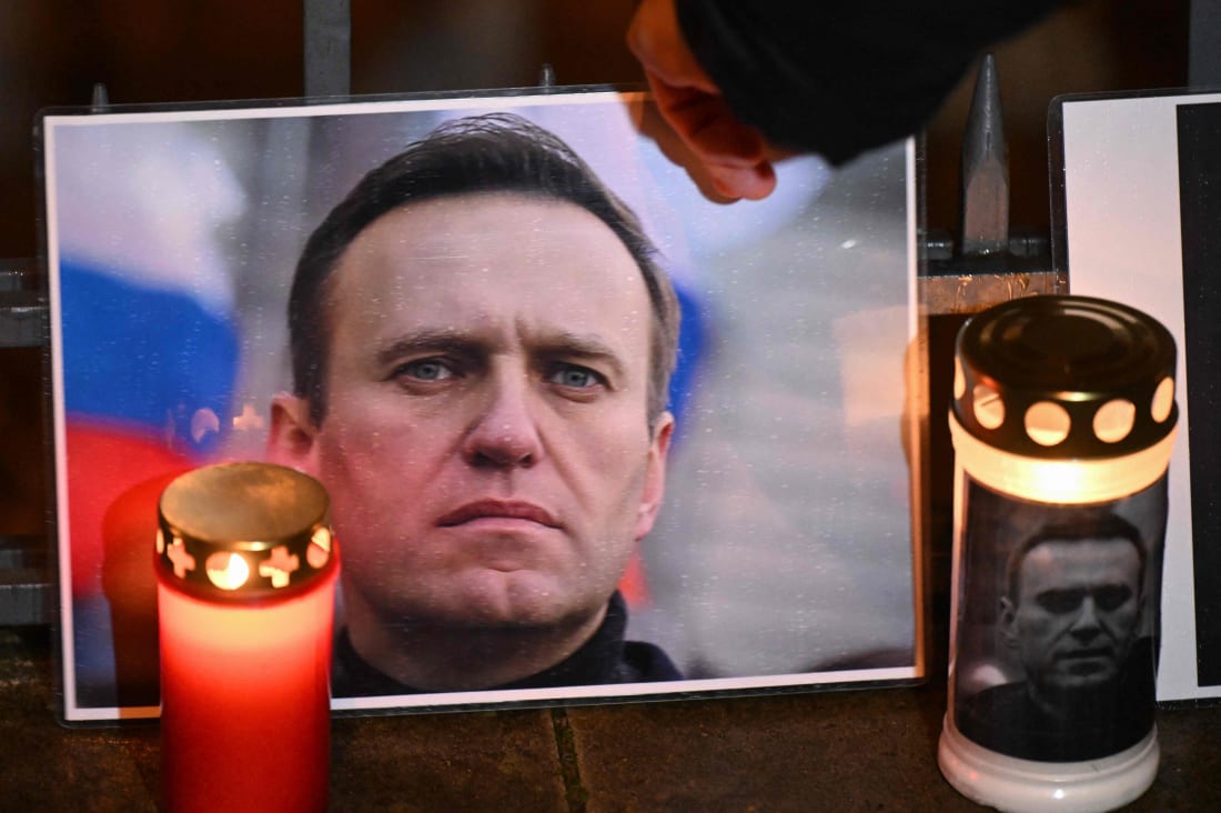 En hand ställer upp inplastad bild av Aleksej Navalnyj intill ljus, bland annat ett med en bild av Navalnyj.