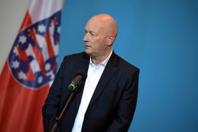 Thomas Kemmerich tittar åt sidan och står framför en mikrofon. I bakgrunden syns en flagga mot en ljusblå vägg.