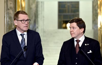 Matti Vanhanen och Anders Norlén iklädda mörka kostymer under en presskonferens i rikssalen i Finlands riksdag. 