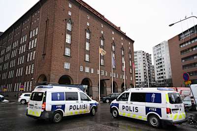 Två polisbilar parkerade utanför ett stort brunt tegelhus inne i en stad. 