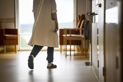 Anonym vårdare i vit sjukhusrock promenerar i korridor
