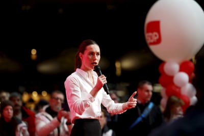 Sanna Marin med allvarlig min håller tal på valkampanjtillfälle, med SDP-ballonger i bakgrunden