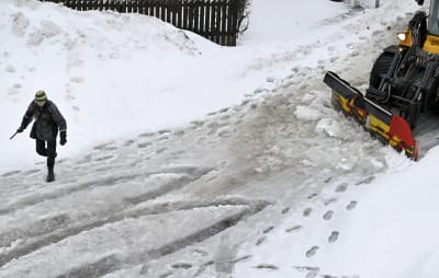 En person går på en snöslaskig gata som plogas.