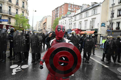 En maskerad demonstrant med sköld står på en gata i Paris. Bakom demonstranten syns en rad kravallpoliser.