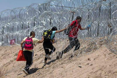 Invandrare går igenom raktråd som omger ett provisoriskt migrantläger i El Paso.