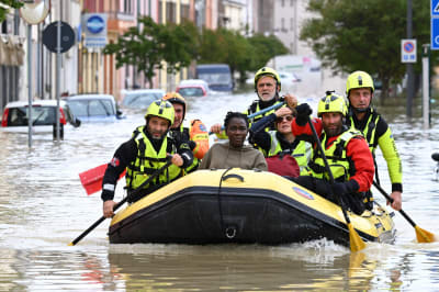 Räddningspersonal paddlar i en gummibåt på en översvämmad gata.