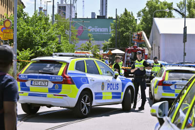 Poliser och polisbilar som står utanför ett nöjesfält. Det är soligt.