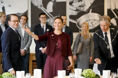 Kronprinsessan Victoria står mellan prins Daniel och Hankens rektor Ingmar Björkman, gestikulerar med ena handen och ser glad ut.