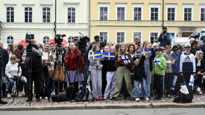 Journalister med kameror står intill en stor grupp med vuxna och barn på torget i Lovisa. En del av barnen håller i svenska flaggor, andra har finska flaggor i händerna.