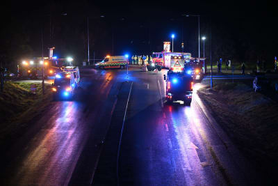 En stor mängd ambulanser och brandbilar står vid en korsning i mörkret. Flera av dem har sirenerna på. Vid vägen står också brandmän och annan räddningspersonal.