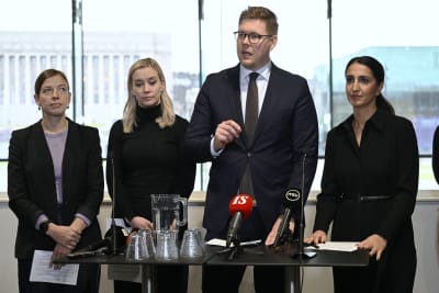 Representanter för oppositionspartierna står bakom ett bord med mikrofoner. 