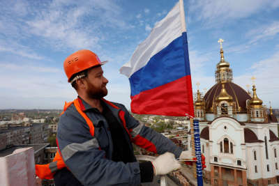 En man hissar ryska flaggan i Mariupol, i fonden en kyrka.